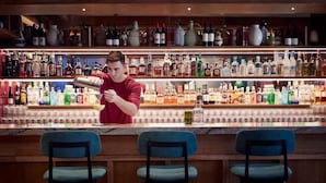 Een bar met flessen drank op de planken en een bartender die een drankje bereidt.