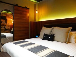 A modern hotel room with a large bed, wooden headboard, and a mirror with a brick wall design. - Boutique Hotel Cadillac (Mexico City)