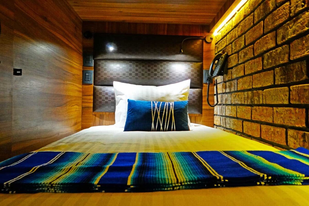 A room with a bed, a brick wall, and a wooden ceiling.