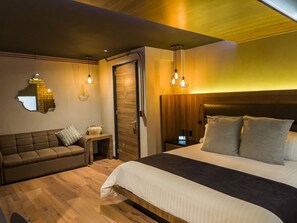 A modern bedroom with a wooden headboard, a large bed, a sofa, and a nightstand with a lamp. - Boutique Hotel Cadillac (Mexico City)