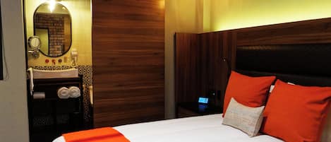 Hotellihuone, jossa on sänky, puinen pääty, yöpöytä, peili, pesuallas ja pyyhekoukku.