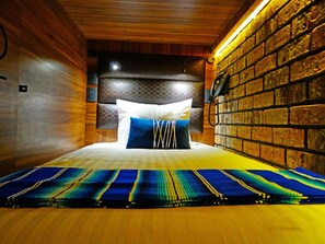 A bed with a patterned bedspread, a headboard with a textured design, and a brick wall on one side. - Boutique Hotel Cadillac (Mexico City)