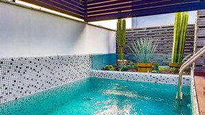 A swimming pool with a tiled edge, surrounded by various plants and a wooden pergola. - Boutique Hotel Cadillac (Mexico City)