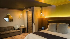 A modern bedroom with a wooden headboard, a large bed, a sofa, and a nightstand with a lamp. - Boutique Hotel Cadillac (Mexico City)