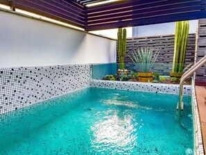 A swimming pool with a tiled edge, surrounded by various plants and a wooden pergola. - Boutique Hotel Cadillac (Mexico City)