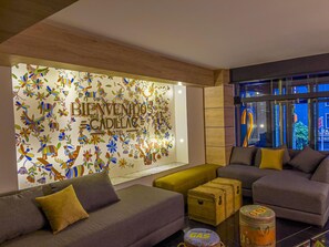 A modern hotel lobby with a colorful wall mural, comfortable seating, and a vintage suitcase on a table. - Boutique Hotel Cadillac (Mexico City)