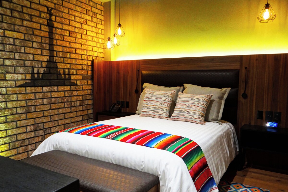 A hotel room with a brick wall, wooden headboard, and a colorful striped bedspread.