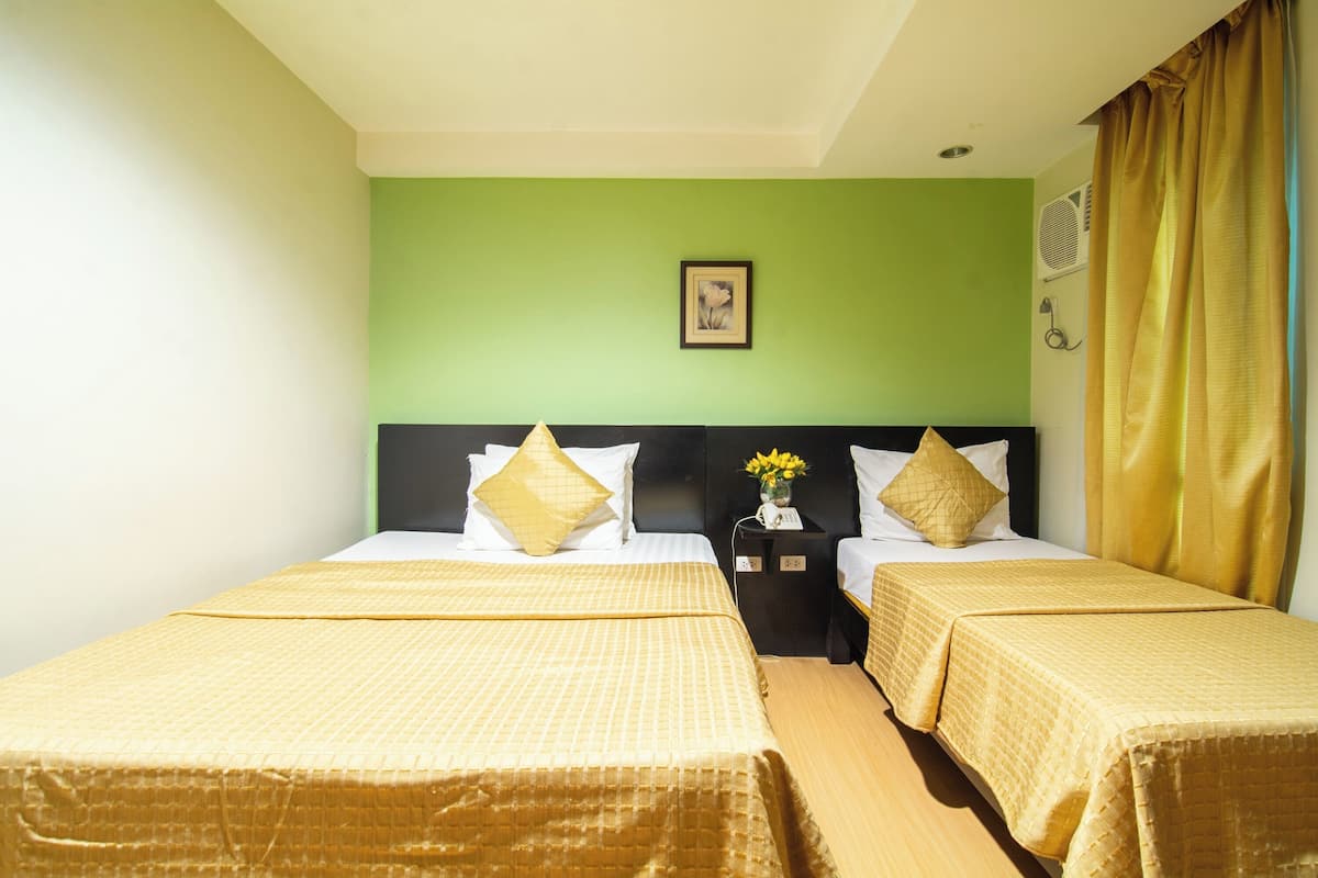 Habitación de hotel con dos camas, paredes verdes, un cuadro enmarcado, una mesita de noche con un teléfono y una ventana con cortinas.