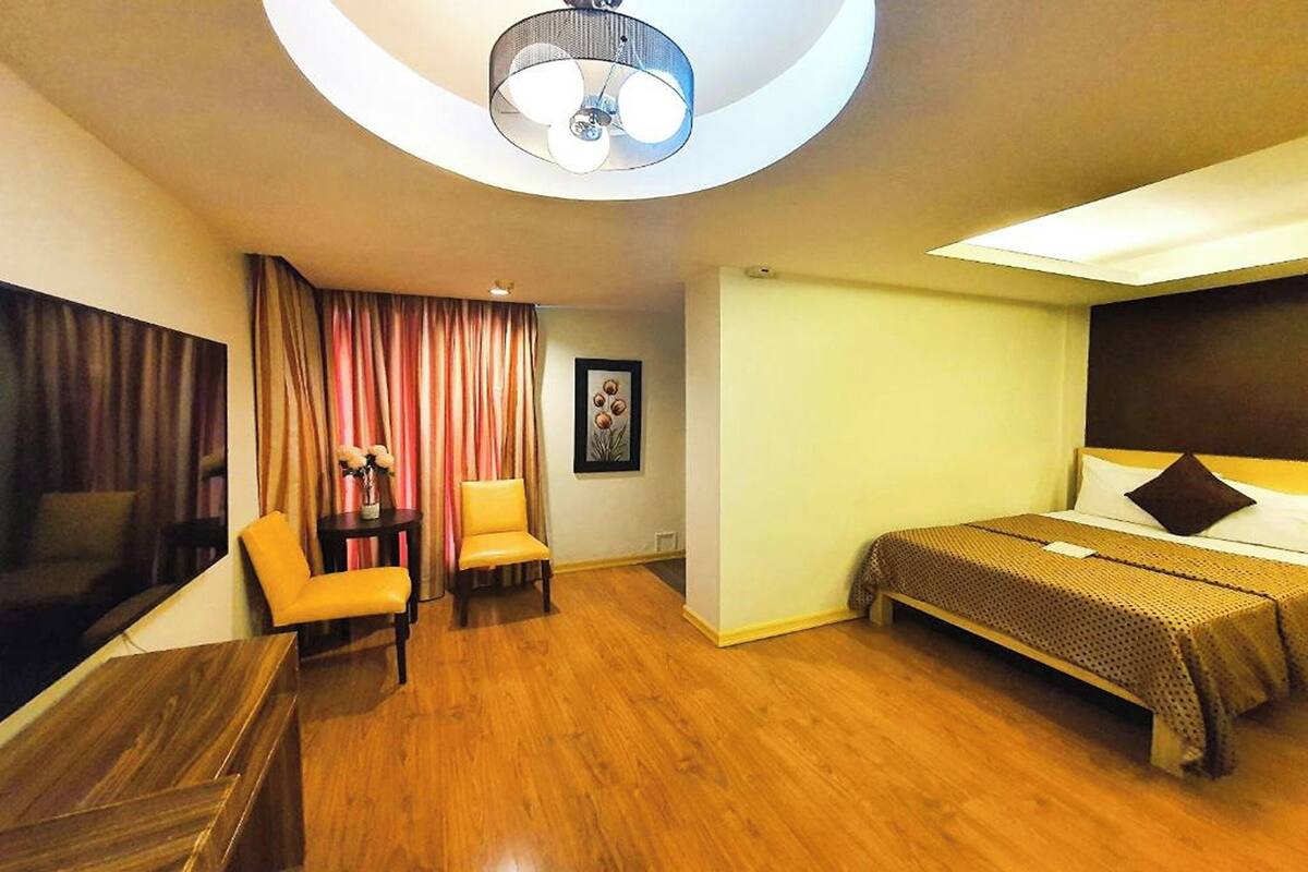 Una habitación de hotel con cama, escritorio, silla, luz de techo y ventana con cortinas.