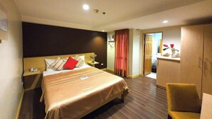 A hotel room with a large bed, a bedside table with a lamp, a wardrobe, and a small seating area. - Festive Hotel Makati (Makati)