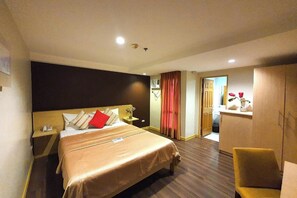 Une chambre d’hôtel avec un grand lit, une table de chevet avec une lampe, une armoire et un petit coin salon.