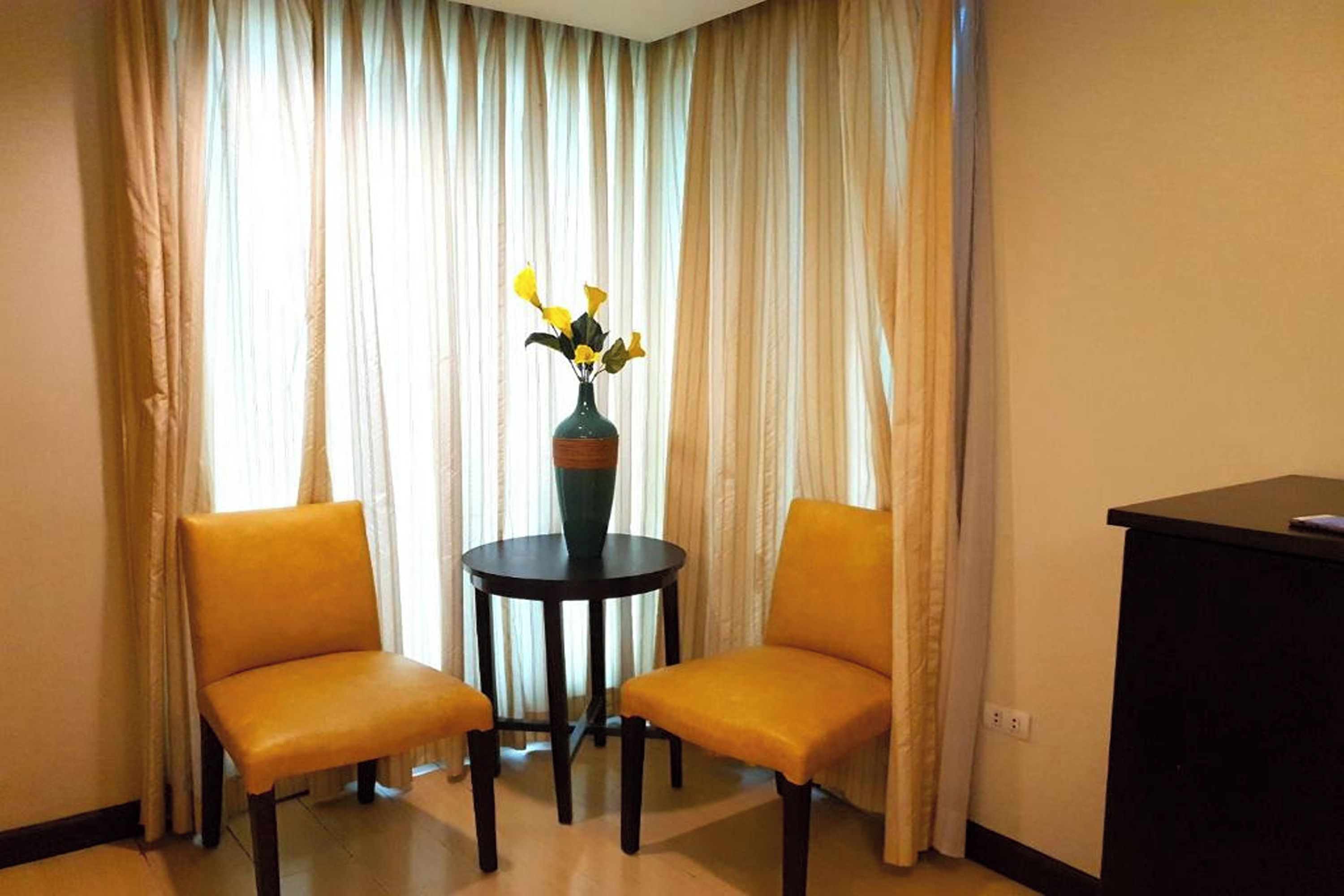 Una habitación con dos sillas amarillas alrededor de una pequeña mesa con un jarrón de flores amarillas.