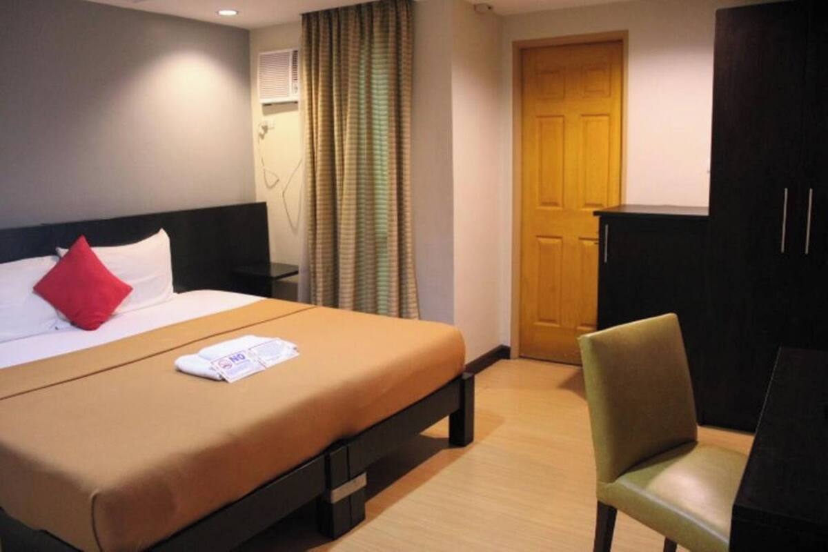 Una habitación de hotel con una cama, un escritorio, una silla, un armario y una puerta.