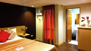 A hotel room with a bed, a nightstand with a vase, a red curtain, and a wooden door leading to a bathroom. - Festive Hotel Makati (Makati)