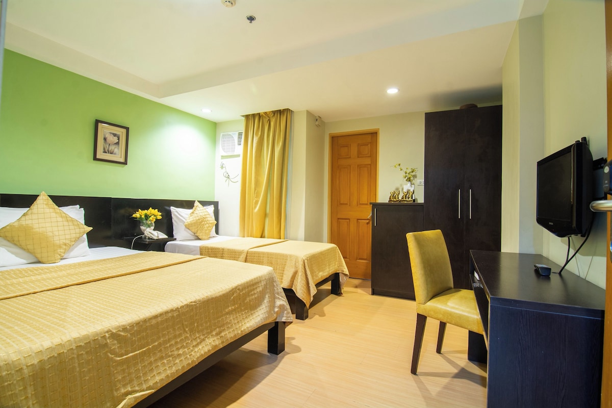 A hotel room with two beds, a desk, a chair, a television, and a wardrobe.