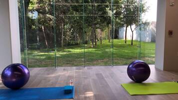 Una habitación con un amplio ventanal, suelo de madera, dos pelotas de ejercicio y colchonetas de yoga.