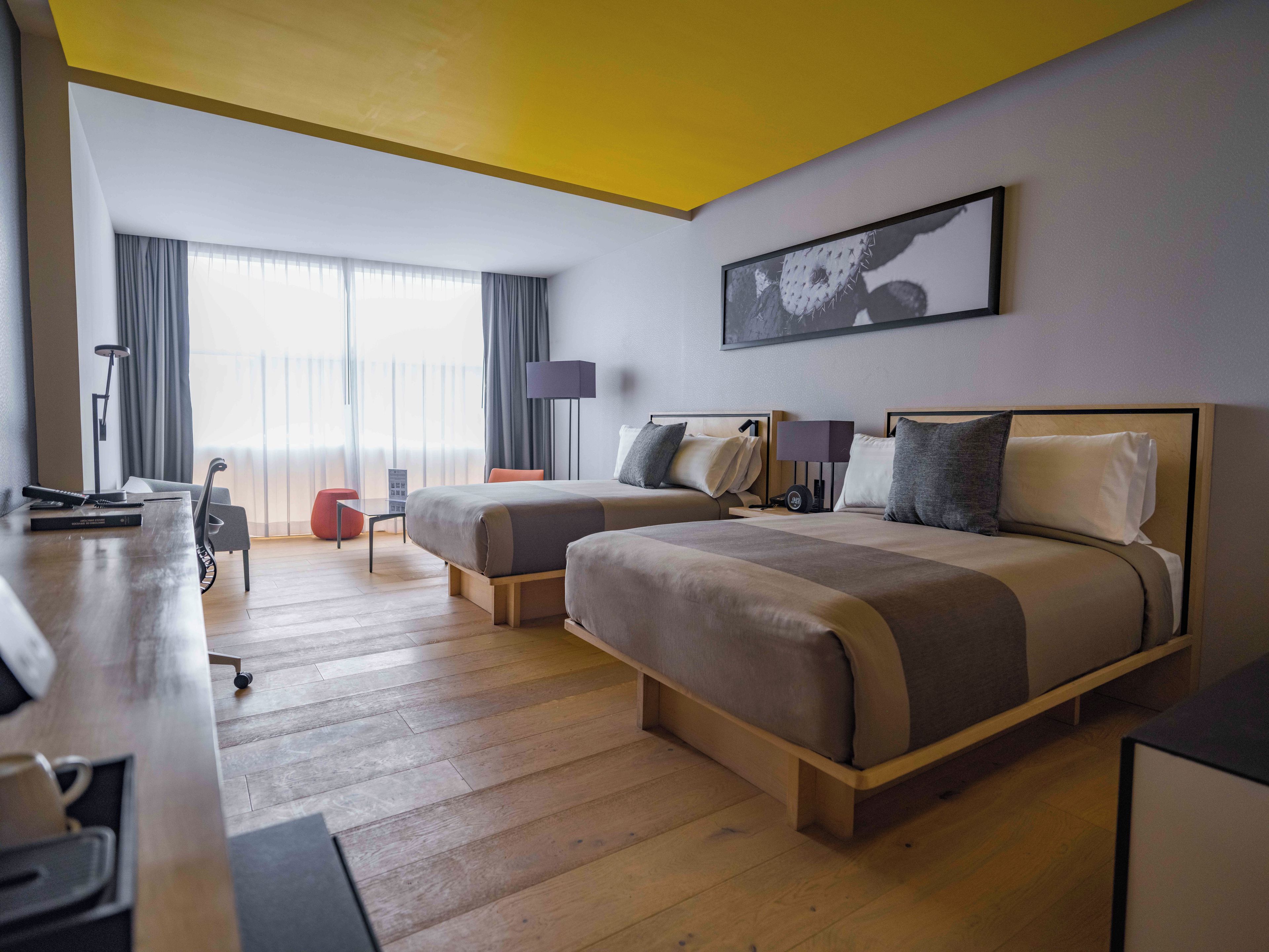 Een hotelkamer met twee bedden, een bureau, een lamp en een groot raam met gordijnen.