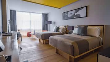 Een hotelkamer met twee bedden, een bureau, een lamp en een groot raam met gordijnen.