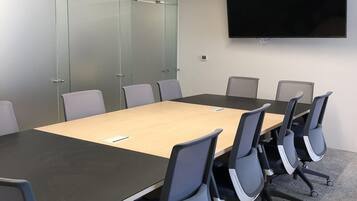 A conference room with a long table, six chairs, a flat-screen TV, and glass walls.