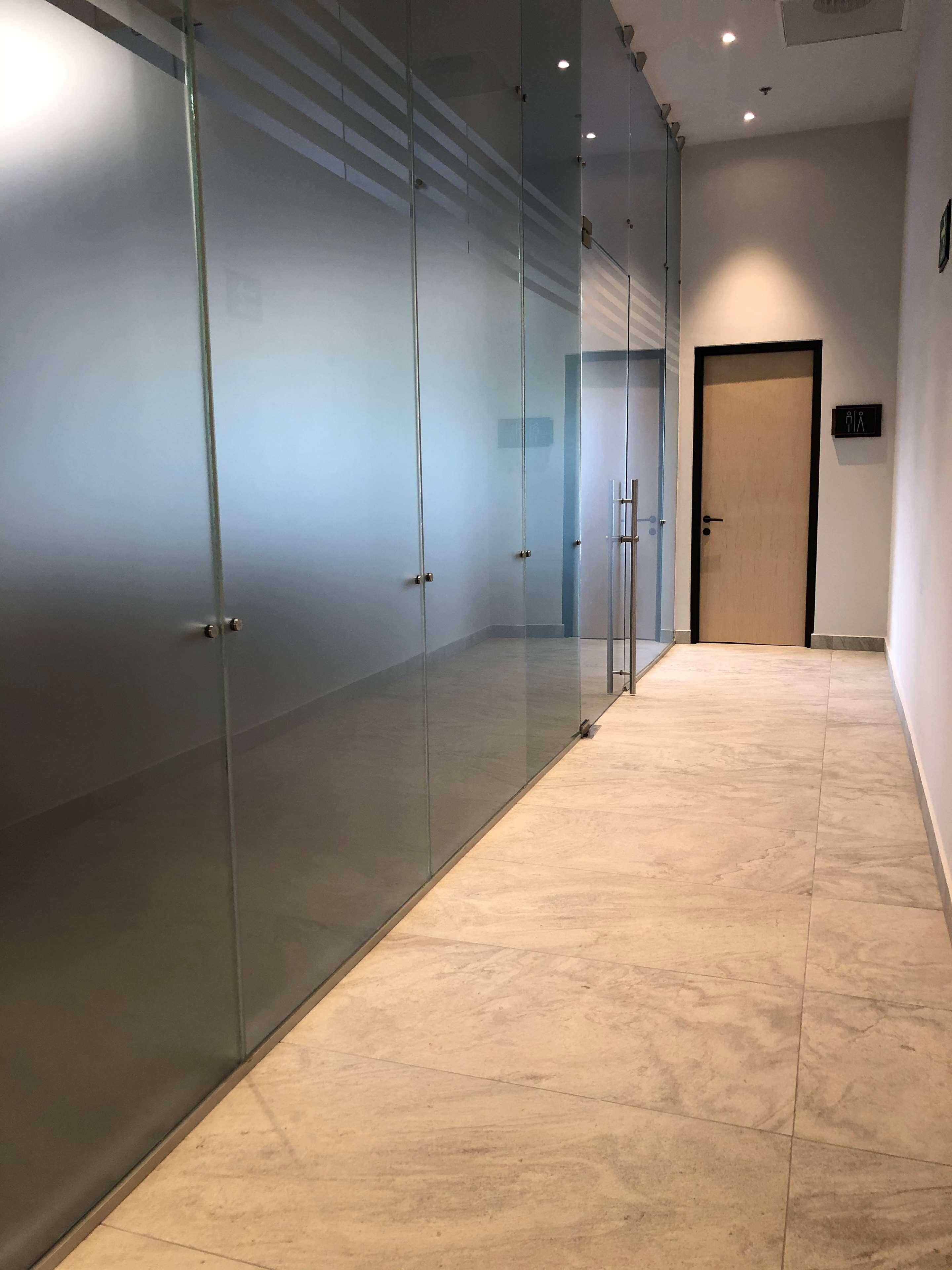 Un pasillo con puertas de vidrio esmerilado, suelo de baldosas y una puerta con un letrero que indica un baño.