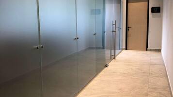 Un pasillo con puertas de vidrio esmerilado, suelo de baldosas y una puerta con un letrero que indica un baño.