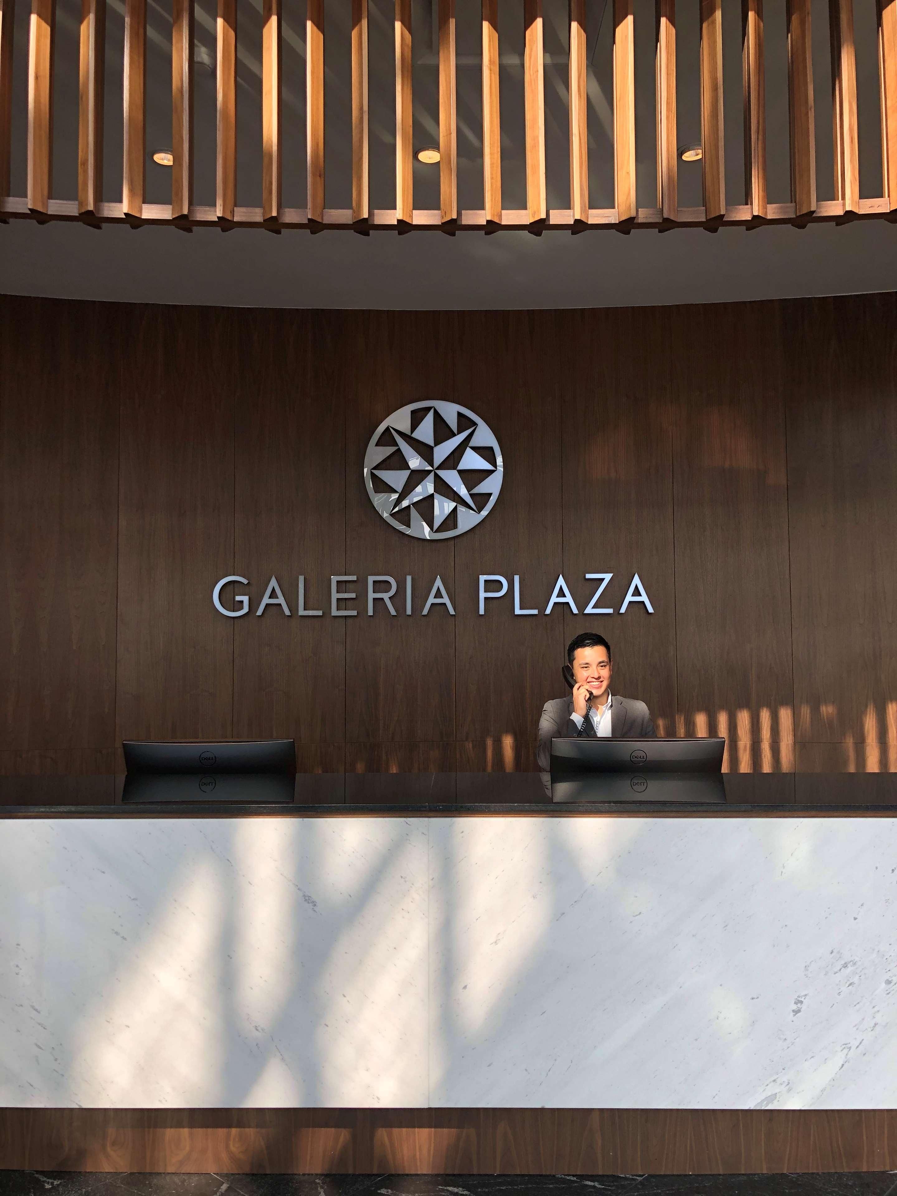 A reception desk with a logo above it and the name 'GALERIA PLAZA' on the wall.