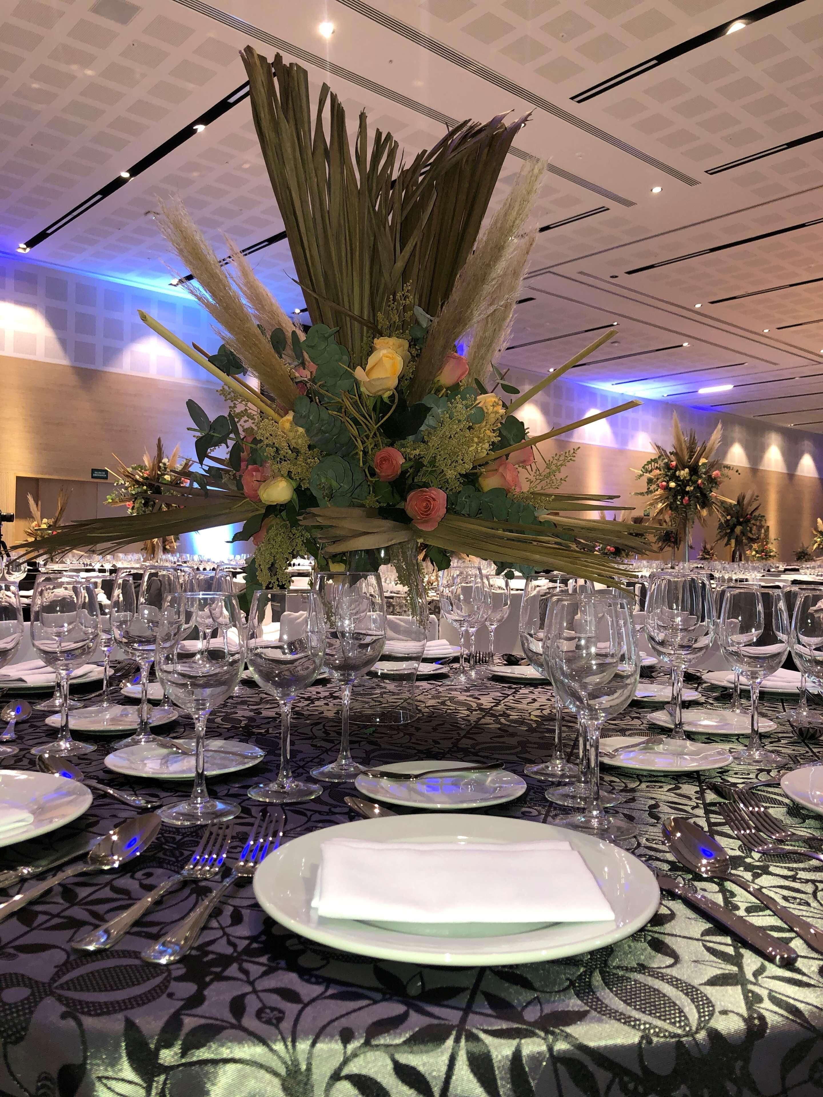 A banquet table set with wine glasses, plates, and cutlery, surrounded by a decorative floral arrangement.