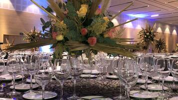 A banquet table set with wine glasses, plates, and cutlery, surrounded by a decorative floral arrangement.