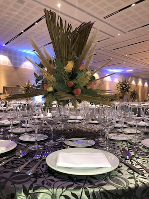 A banquet table set with wine glasses, plates, and cutlery, surrounded by a decorative floral arrangement. - Galeria Plaza San Jeronimo (Mexico City)