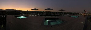 A rooftop pool area with multiple pools, umbrellas, and lounge chairs.