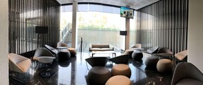 A modern lobby with a curved ceiling, a glass wall, and a seating area with contemporary chairs and ottomans. - Galeria Plaza San Jeronimo (Mexico City)