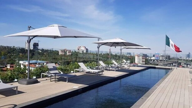 A rooftop pool area with lounge chairs and umbrellas, a flag, and a cityscape in the background. - Galeria Plaza San Jeronimo (Mexico City)
