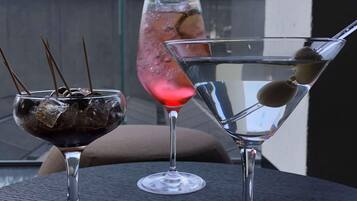 Três copos com bebidas sobre uma mesa, com vista para árvores e edifícios ao fundo.