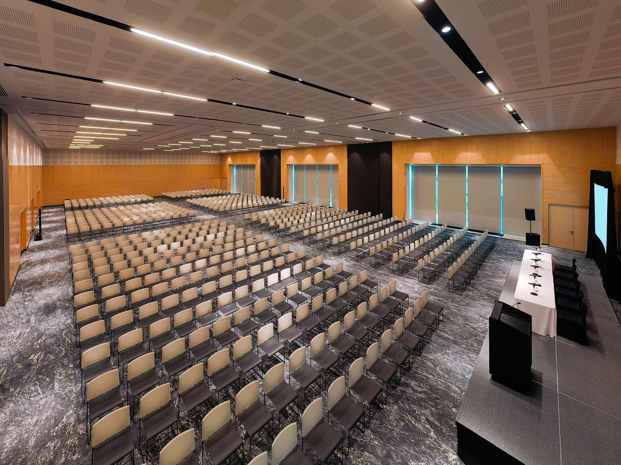 A large conference room with rows of chairs, a stage with a podium, and a carpeted floor.