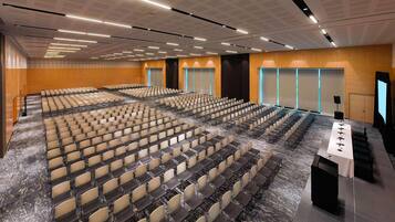 A large conference room with rows of chairs, a stage with a podium, and a carpeted floor.
