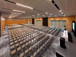 A large conference room with rows of chairs, a stage with a podium, and a carpeted floor. - Galeria Plaza San Jeronimo (Mexico City)