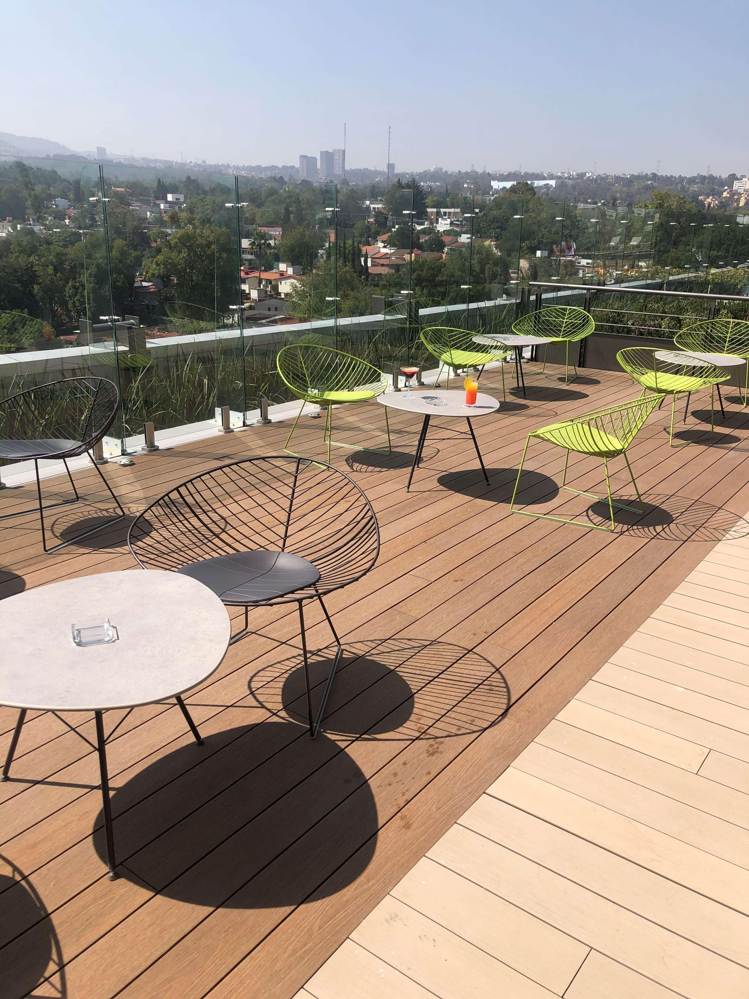 A rooftop terrace with outdoor seating, including round tables and chairs, and a view of the cityscape in the background.