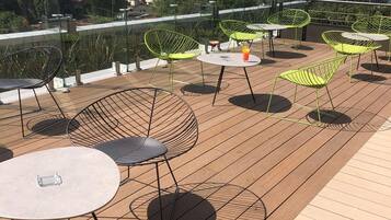 A rooftop terrace with outdoor seating, including round tables and chairs, and a view of the cityscape in the background.