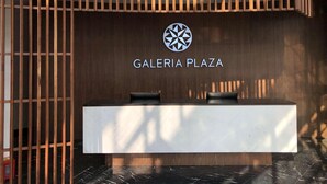 A reception desk with a logo above it, wooden slats on the left, and a marble floor. - Galeria Plaza San Jeronimo (Mexico City)