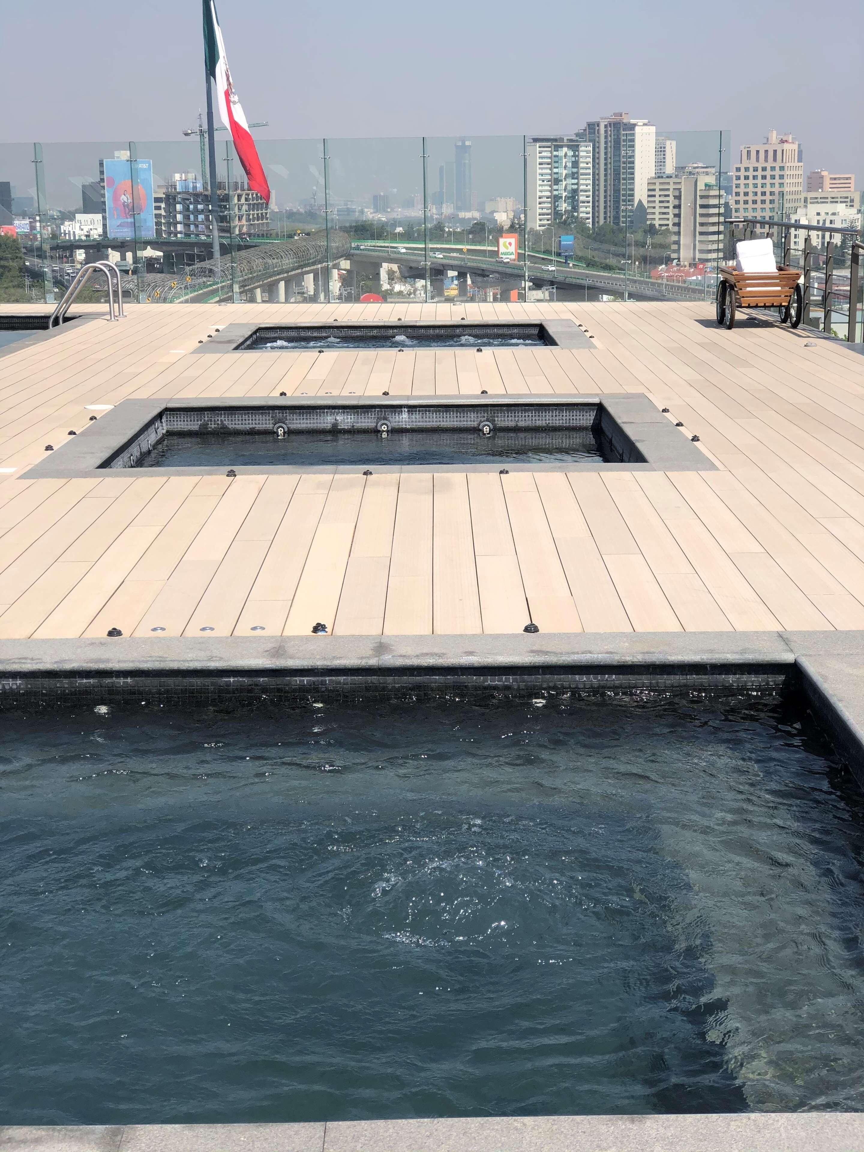 A rooftop pool area with multiple water features and a view of the city skyline.