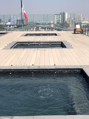 A rooftop pool area with multiple water features and a view of the city skyline. - Galeria Plaza San Jeronimo (Mexico City)