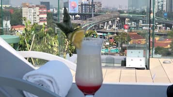 A glass of red drink with a lemon slice on a table, a bowl of snacks, and a view of a cityscape with buildings and a flag.