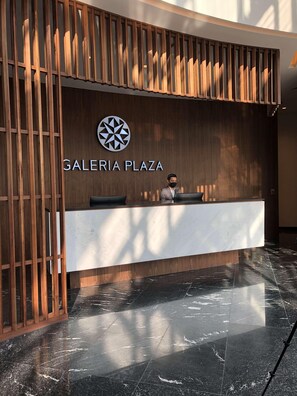 Un comptoir d’accueil à la Galeria Plaza, doté d’un design moderne, avec un logo placé au-dessus du nom et une personne derrière.