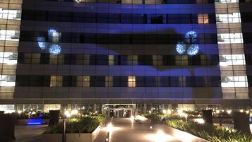 A modern building with a glass facade, illuminated by internal lighting and blue decorative lights.