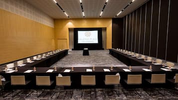 Un salón de conferencias con una larga mesa y sillas, una pantalla de proyector y piso alfombrado.
