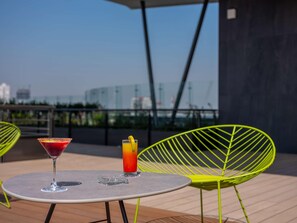A table with two drinks and a chair on an outdoor terrace with a view of buildings. - Galeria Plaza San Jeronimo (Mexico City)