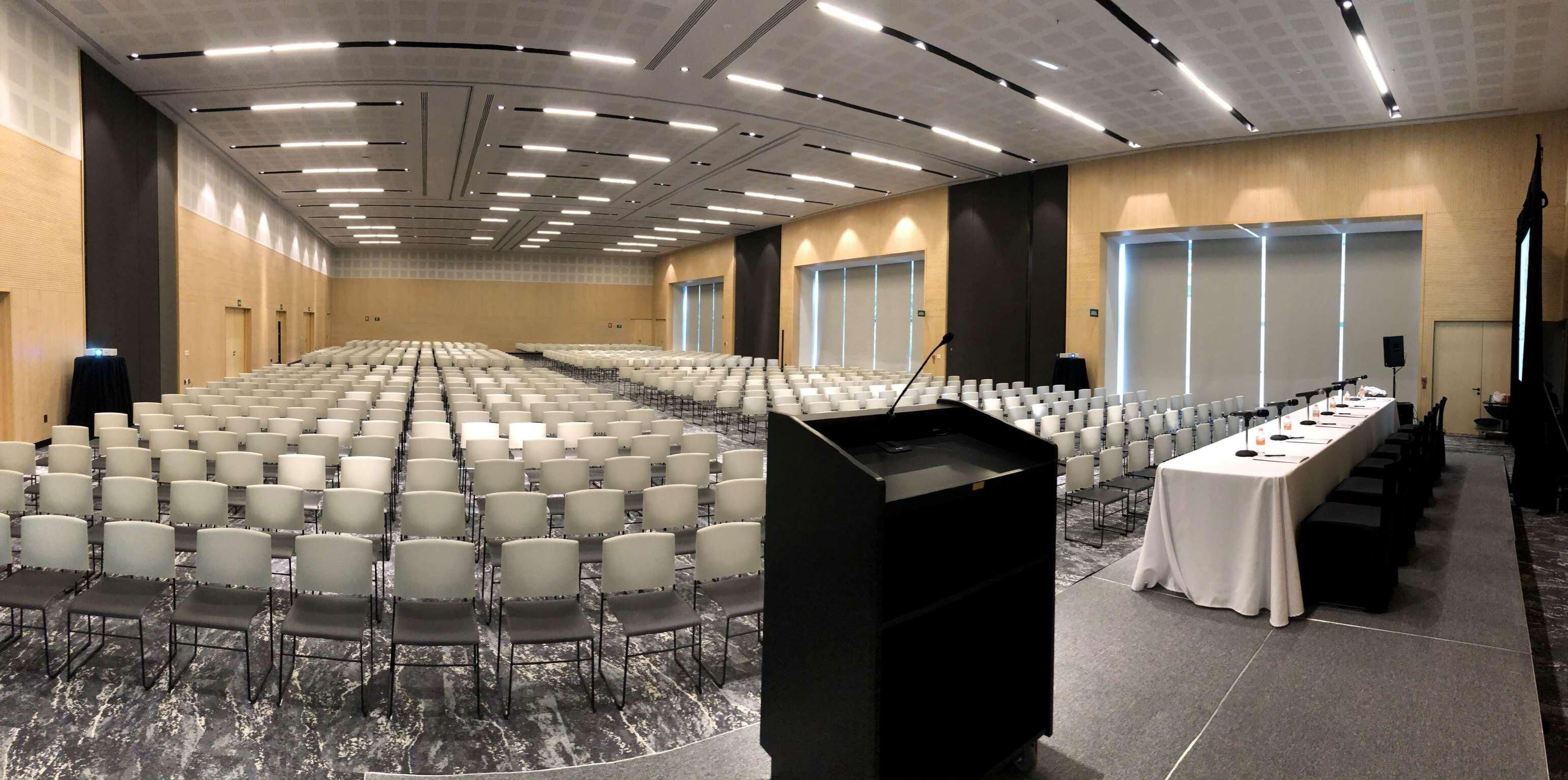A large conference room with rows of chairs, a podium, and a table with chairs.
