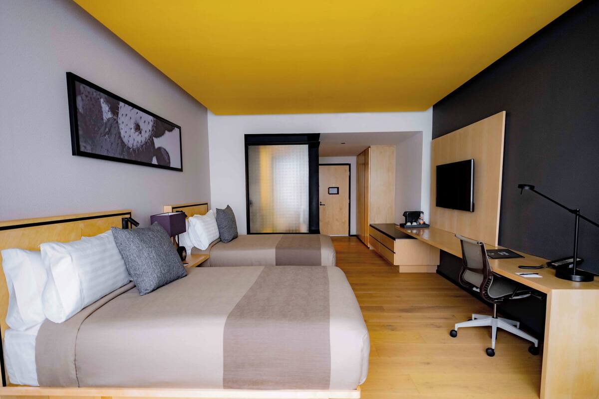 Une chambre d’hôtel moderne équipée de deux lits, d’un bureau, d’une chaise, d’une télévision et d’une porte donnant sur une autre chambre.