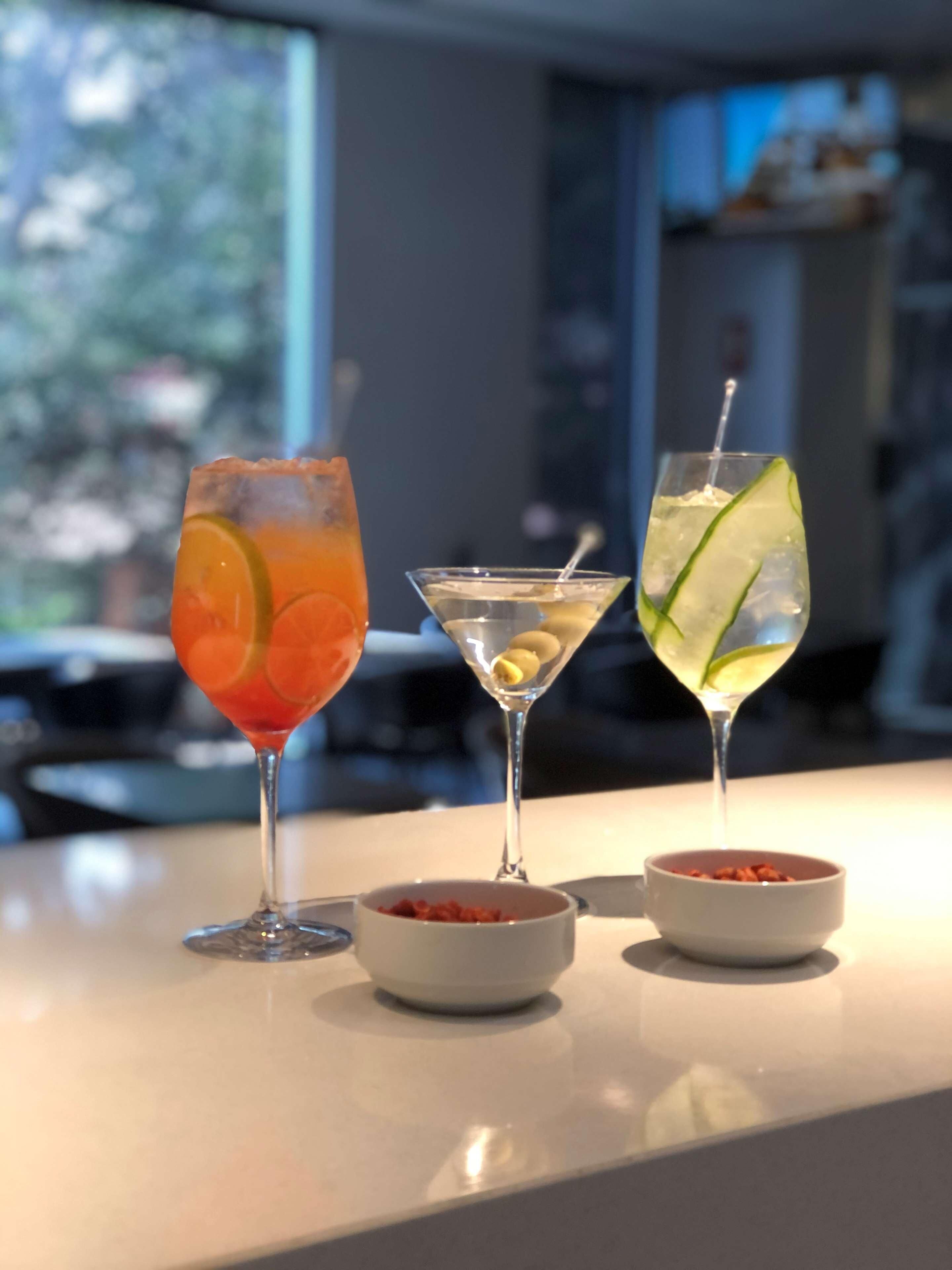 Drie cocktails op een barkruk met twee kleine schaaltjes garnering.