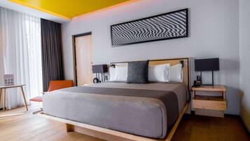 Une chambre d’hôtel moderne avec un grand lit, une tête de lit en bois, deux tables de chevet avec des lampes, un petit bureau et une chaise.